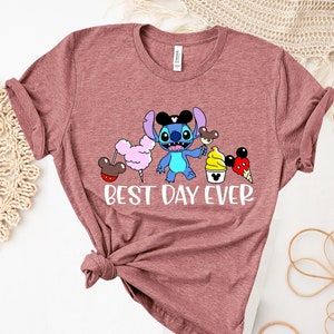 May include: A maroon t-shirt with a cartoon image of Stitch from Lilo & Stitch wearing Mickey Mouse ears and holding a Mickey Mouse ice cream cone. The text "BEST DAY EVER" is printed below the image.