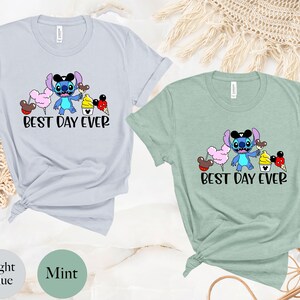 May include: Two t-shirts with a blue Stitch character holding a Mickey Mouse ice cream cone. The text "Best Day Ever" is printed on both shirts. One shirt is light blue and the other is mint green.