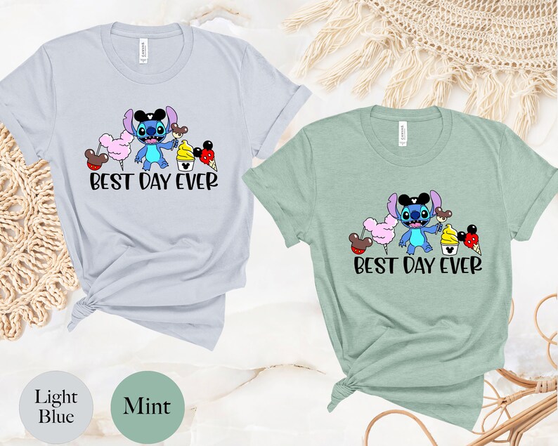 May include: Two t-shirts with a blue Stitch character holding a Mickey Mouse ice cream cone. The text "Best Day Ever" is printed on both shirts. One shirt is light blue and the other is mint green.