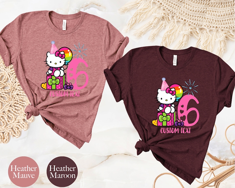 May include: Two t-shirts with a Hello Kitty design. The shirt on the left is heather mauve and the shirt on the right is heather maroon. Both shirts feature Hello Kitty wearing a party hat and holding a balloon. The number 6 is printed on both shirts. The text "CUSTOM TEXT" is printed on both shirts.