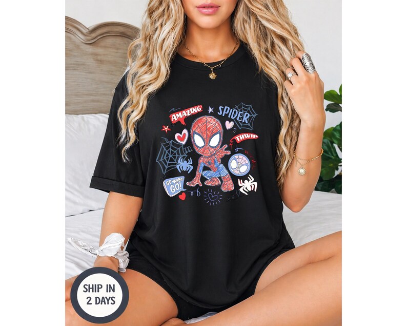 Puede incluir: Camiseta negra con un dise&ntilde;o de dibujos animados de Spider-Man. El gr&aacute;fico incluye las palabras "Amazing Spider" y elementos de estilo c&oacute;mic como telara&ntilde;as y corazones. La camiseta es de manga corta.