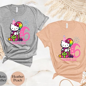 May include: Gray and peach t-shirts with a pink Hello Kitty character wearing a party hat and holding a rainbow balloon. The shirts have a pink number 6 and the text "CUSTOM TEXT".