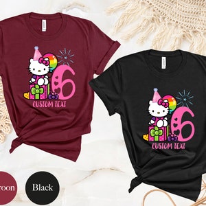 May include: Two t-shirts, one maroon and one black, featuring a cartoon Hello Kitty wearing a party hat and holding a balloon. The shirts have a pink number six and the text "CUSTOM TEXT" printed on them.