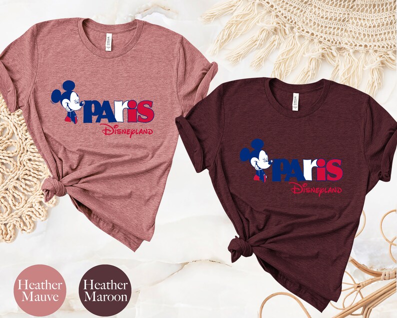 Puede incluir: Dos camisetas con un gr&aacute;fico de Mickey Mouse y el texto "Paris Disneyland". La camiseta de la izquierda es de color malva jaspeado y la camiseta de la derecha es de color marr&oacute;n jaspeado.