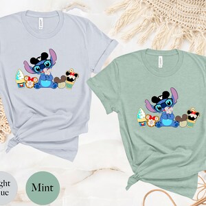 Pode incluir: T-shirts azul claro e verde menta com um personagem de desenho animado com &oacute;culos e gravata borboleta, rodeado de sobremesas. O personagem &eacute; azul com orelhas grandes. As camisas t&ecirc;m as palavras "Light Blue" e "Mint" impressas.