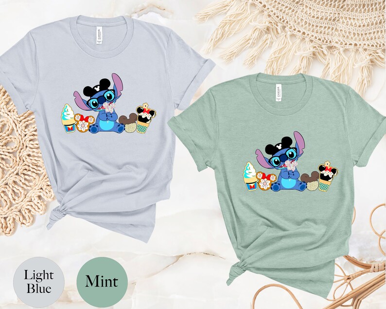 Pode incluir: T-shirts azul claro e verde menta com um personagem de desenho animado com &oacute;culos e gravata borboleta, rodeado de sobremesas. O personagem &eacute; azul com orelhas grandes. As camisas t&ecirc;m as palavras "Light Blue" e "Mint" impressas.