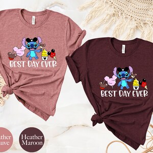 May include: Two t-shirts with a blue Stitch character from Lilo & Stitch holding a Mickey Mouse ice cream cone and other Disney treats. The text on the shirts reads "Best Day Ever". The shirts are available in heather mauve and heather maroon.