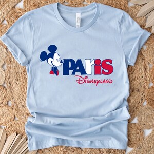 Puede incluir: Camiseta azul claro con un gr&aacute;fico de Mickey Mouse y el texto "Paris Disneyland" en rojo, blanco y azul.