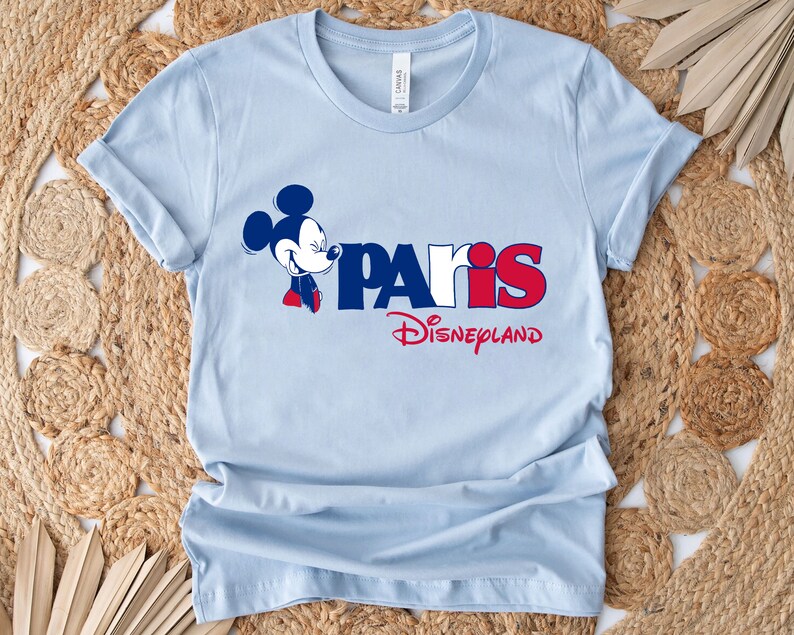Puede incluir: Camiseta azul claro con un gr&aacute;fico de Mickey Mouse y el texto "Paris Disneyland" en rojo, blanco y azul.