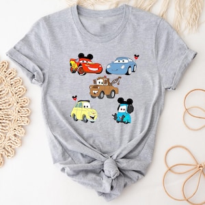 May include: Gray t-shirt with a graphic of five cartoon cars from the Disney Pixar movie Cars. The cars are red, blue, yellow, and brown. Each car has a Mickey Mouse ear on top.