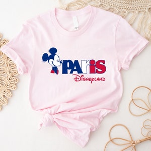 Puede incluir: Camiseta rosa con un gr&aacute;fico azul y rojo de Mickey Mouse y el texto "Paris Disneyland".