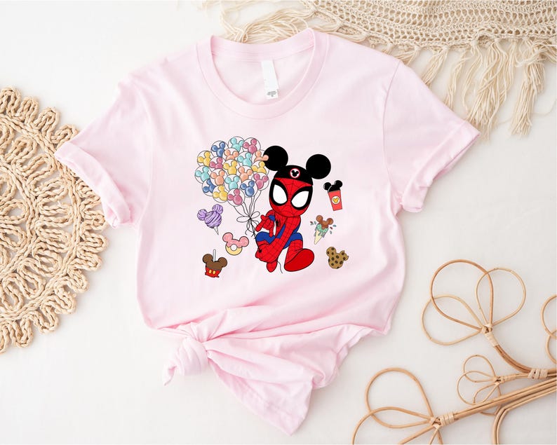 Puede incluir: Una camiseta rosa claro con un personaje de dibujos animados que combina a Spider-Man y Mickey Mouse. El personaje sostiene globos de colores y golosinas. La camiseta est&aacute; anudada en la parte inferior.