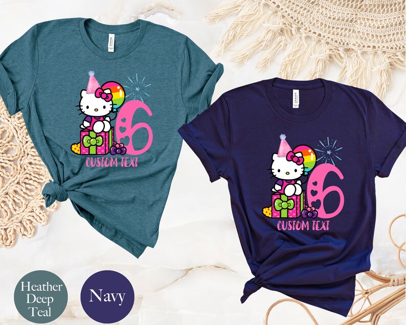 May include: Two t-shirts with a Hello Kitty design. The shirt on the left is teal and the shirt on the right is navy. Both shirts feature Hello Kitty wearing a party hat and holding a balloon. The number 6 is on both shirts. The text "CUSTOM TEXT" is on both shirts.