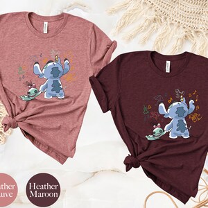 May include: Two t-shirts featuring a cartoon image of Stitch and Angel from Lilo & Stitch. The shirt on the left is heather mauve and the shirt on the right is heather maroon.