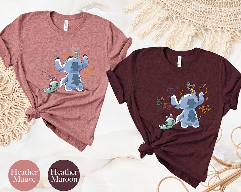 May include: Two t-shirts featuring a cartoon image of Stitch and Angel from Lilo & Stitch. The shirt on the left is heather mauve and the shirt on the right is heather maroon.