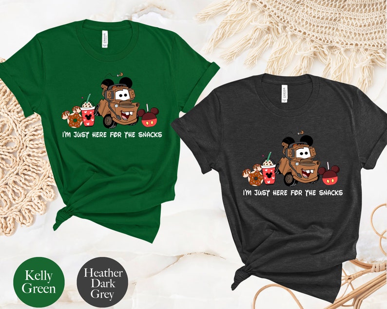 May include: Two t-shirts with a cartoon image of Mater from Cars, a Mickey Mouse head, and snacks. The text on the shirts reads "I'm just here for the snacks". The shirts are available in Kelly Green and Heather Dark Grey.