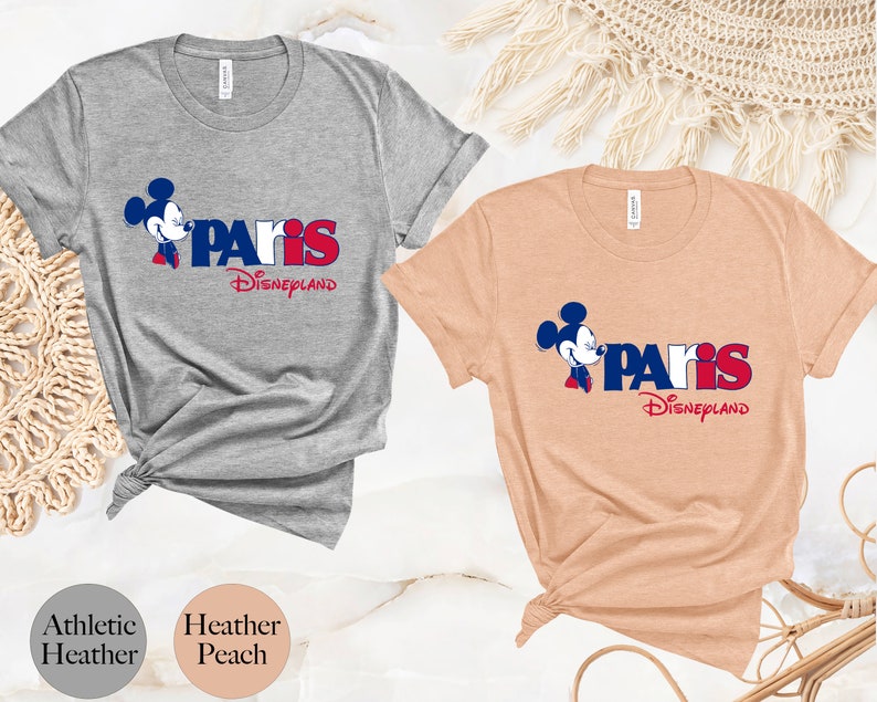 Puede incluir: Dos camisetas con un gr&aacute;fico de Mickey Mouse y el texto "Paris Disneyland". La camiseta de la izquierda es gris deportivo jaspeado y la camiseta de la derecha es melocot&oacute;n jaspeado.