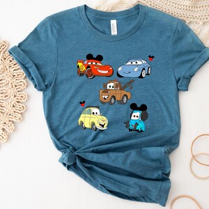 May include: A teal blue t-shirt with a graphic print of five cartoon cars from the Disney Pixar movie Cars. The cars include Lightning McQueen, Mater, Francesco Bernoulli, and two other cars.
