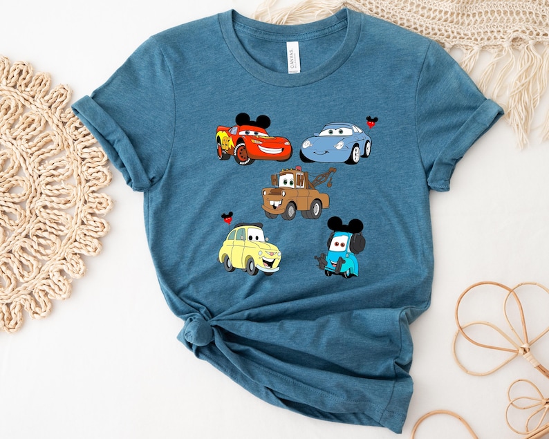 May include: A teal blue t-shirt with a graphic print of five cartoon cars from the Disney Pixar movie Cars. The cars include Lightning McQueen, Mater, Francesco Bernoulli, and two other cars.
