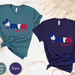 Puede incluir: Dos camisetas con un gr&aacute;fico de Mickey Mouse y el texto "Paris Disneyland". La camiseta de la izquierda es de color azul oscuro jaspeado y la camiseta de la derecha es azul marino.