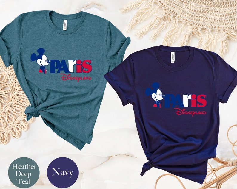 Puede incluir: Dos camisetas con un gr&aacute;fico de Mickey Mouse y el texto "Paris Disneyland". La camiseta de la izquierda es de color azul oscuro jaspeado y la camiseta de la derecha es azul marino.