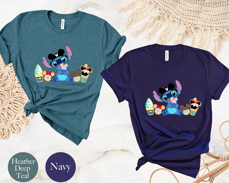 Pode incluir: Duas camisetas, uma verde-azulado escuro e outra azul marinho, cada uma com um personagem de desenho animado Stitch usando &oacute;culos e um chap&eacute;u com orelhas do Mickey Mouse. O personagem &eacute; cercado por sobremesas, incluindo sorvetes e cupcakes.