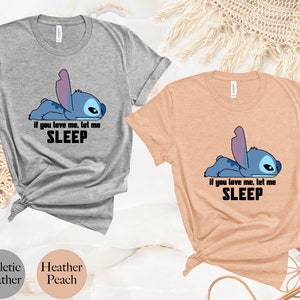 K&ouml;nnte beinhalten: Zwei T-Shirts mit einem blauen Stitch-Charakter aus Lilo & Stitch. Der Text auf den Shirts lautet "Wenn du mich liebst, lass mich schlafen". Die Shirts sind in den Farben Heidelbeer-Peach und Sport-Heather erh&auml;ltlich.