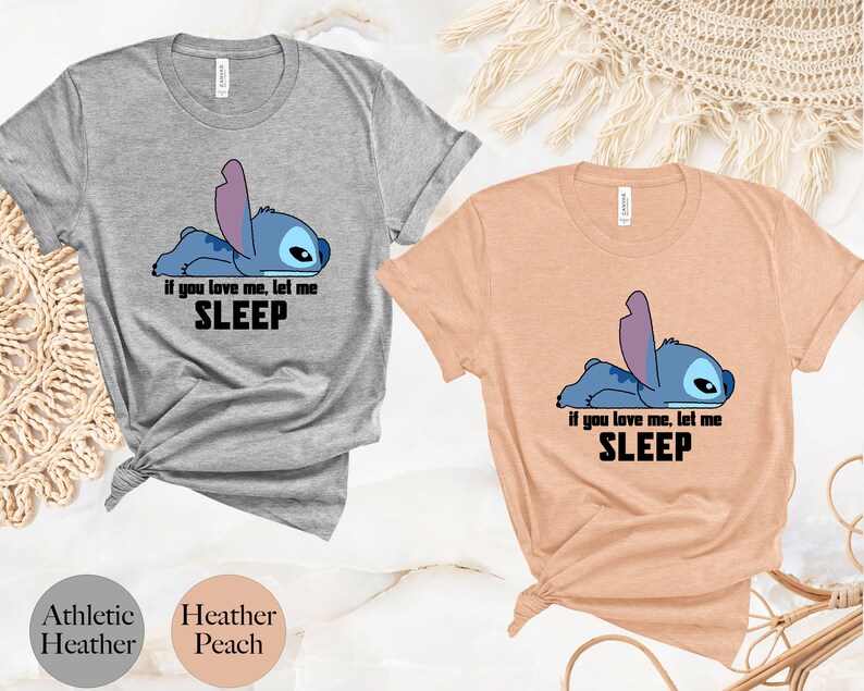 K&ouml;nnte beinhalten: Zwei T-Shirts mit einem blauen Stitch-Charakter aus Lilo & Stitch. Der Text auf den Shirts lautet "Wenn du mich liebst, lass mich schlafen". Die Shirts sind in den Farben Heidelbeer-Peach und Sport-Heather erh&auml;ltlich.