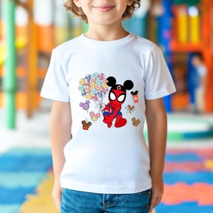 Puede incluir: Camiseta blanca con un personaje de dibujos animados que combina a Spider-Man y Mickey Mouse. El personaje sostiene globos de colores. Otros gr&aacute;ficos incluyen una galleta, helado y una bebida. La camiseta la lleva un ni&ntilde;o.