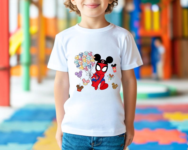 Puede incluir: Camiseta blanca con un personaje de dibujos animados que combina a Spider-Man y Mickey Mouse. El personaje sostiene globos de colores. Otros gr&aacute;ficos incluyen una galleta, helado y una bebida. La camiseta la lleva un ni&ntilde;o.