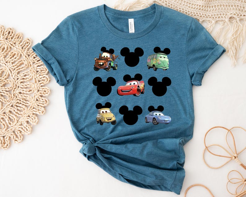 Pu&ograve; includere: Una maglietta blu turchese con una stampa grafica di orecchie di Topolino e personaggi di Cars. I personaggi di Cars includono Saetta McQueen, Cricchetto e un'auto da corsa blu.