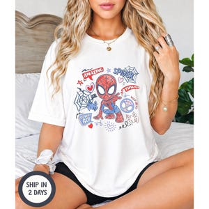 Puede incluir: Camiseta blanca con un dise&ntilde;o de Spider-Man de dibujos animados. El gr&aacute;fico incluye las palabras "Amazing", "Spider", "Thwip" y "Go!" junto con telara&ntilde;as, corazones y garabatos. La camiseta es de estilo casual y c&oacute;modo.