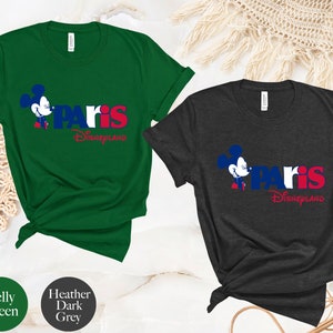 Puede incluir: Dos camisetas con un gr&aacute;fico de Mickey Mouse y el texto "Paris Disneyland". La camiseta de la izquierda es verde Kelly y la camiseta de la derecha es gris oscuro jaspeado.