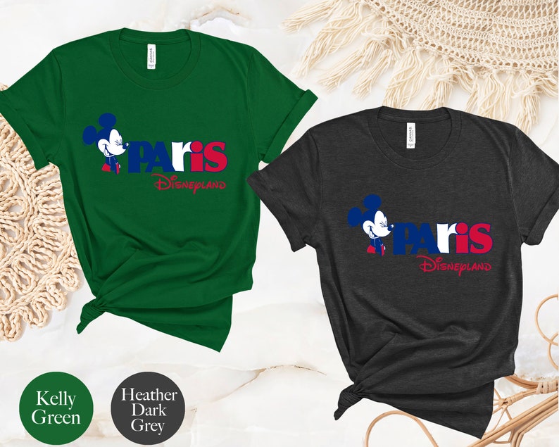 Puede incluir: Dos camisetas con un gr&aacute;fico de Mickey Mouse y el texto "Paris Disneyland". La camiseta de la izquierda es verde Kelly y la camiseta de la derecha es gris oscuro jaspeado.