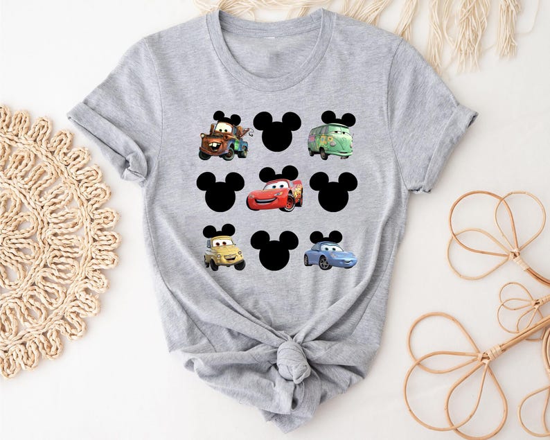 Pu&ograve; includere: Maglietta grigia con un design di Topolino con vari personaggi di Cars, tra cui Saetta McQueen, Cricchetto e Cricchetto il carro attrezzi.