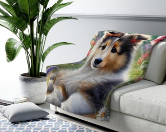 May include: A soft, plush throw blanket featuring a colorful illustration of a Collie dog lying in a field of flowers. The dog has brown, black, and white fur and is looking directly at the viewer.
