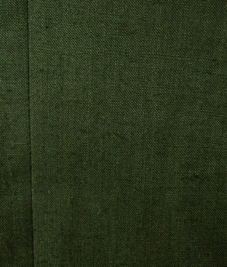 May include: Close-up of a textured, dark green fabric. The fabric has a woven appearance with visible threads, creating a slightly rough surface. A vertical seam runs down the left side, adding a subtle design element.