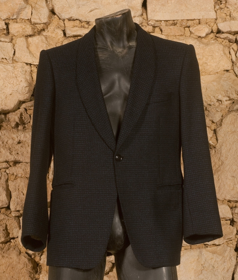 May include: A dark blue blazer with a subtle pattern. The blazer has a single button closure and a notched lapel.