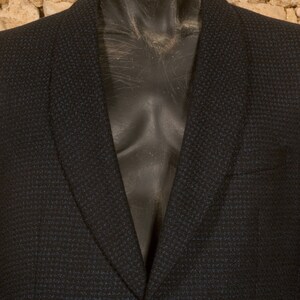 May include: A dark blue blazer with a textured pattern. The blazer has a notched lapel and a single button closure.