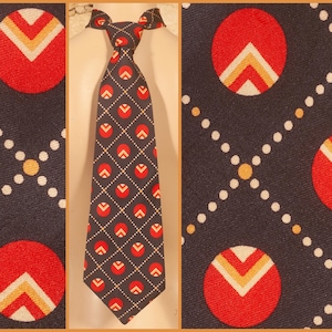 Puede incluir: Una corbata azul marino con un patrón repetido de círculos rojos con diseños de chevron blancos y amarillos. La corbata también presenta un patrón de diamantes con detalles en rojo y blanco.