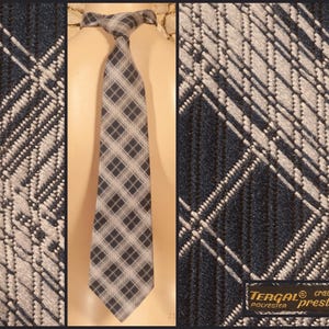 Peut inclure: Une cravate présentant un motif à carreaux bleu marine foncé et blanc avec une texture tissée en diagonale. La cravate est présentée sur un torse de mannequin. Une étiquette rectangulaire indique Tergal cravate prestige polyester.