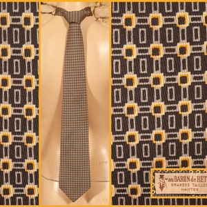 Peut inclure: Une cravate avec un motif géométrique répétitif composé de carrés et de rectangles gris foncé, gris clair et jaunes. L'étiquette indique "au BARON de RETZ GRANDES TAILLES NANTES" accompagnée d'une petite illustration d'un haut-de-forme.