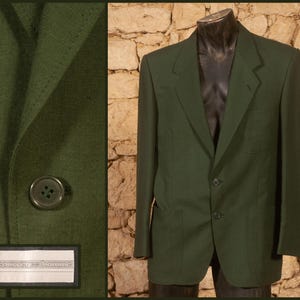 May include: A dark green blazer with two buttons and two front pockets. The blazer is displayed on a mannequin against a stone wall background. The left side of the image shows a close-up of the blazer's fabric and a button.