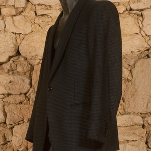 May include: A dark blue blazer with a subtle checkered pattern. The blazer has a single button closure and a flap pocket on the left side.
