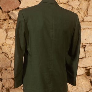 May include: A dark green blazer with a two-button closure, shown from the back. The blazer has a tailored fit and a classic design. The fabric appears to be a solid color, with a subtle texture. The blazer is displayed on a mannequin.