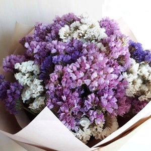 Peut inclure: Un bouquet de fleurs séchées dans des tons de violet, lavande et blanc. Les fleurs sont disposées dans un emballage en papier.
