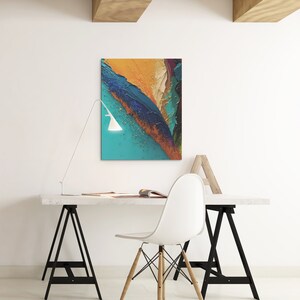May include: A white desk with a white chair and a black lamp. The desk is made of wood and has a white top. The chair is a modern design with a white seat and wooden legs. The lamp is a simple design with a white shade and a black base. There is a painting on the wall behind the desk. The painting is abstract and features a variety of colors, including blue, green, yellow, and orange.