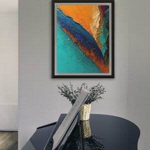 May include: Abstract painting in a black frame with a teal, orange, and blue color scheme. The painting is hanging on a white wall above a black piano.