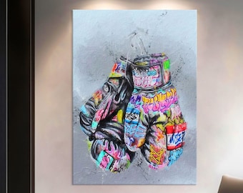 May include: A canvas print featuring a pair of boxing gloves with vibrant graffiti art. The gloves are primarily black with colorful accents of pink, blue, yellow, and green. The background is a textured gray.