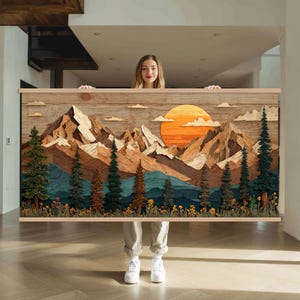 Può includere: Un'opera d'arte paesaggistica in legno raffigurante una catena montuosa, un sole al tramonto e alberi sempreverdi. L'opera d'arte utilizza varie tonalità di marrone, arancione e verde. L'opera d'arte è tenuta da una persona.